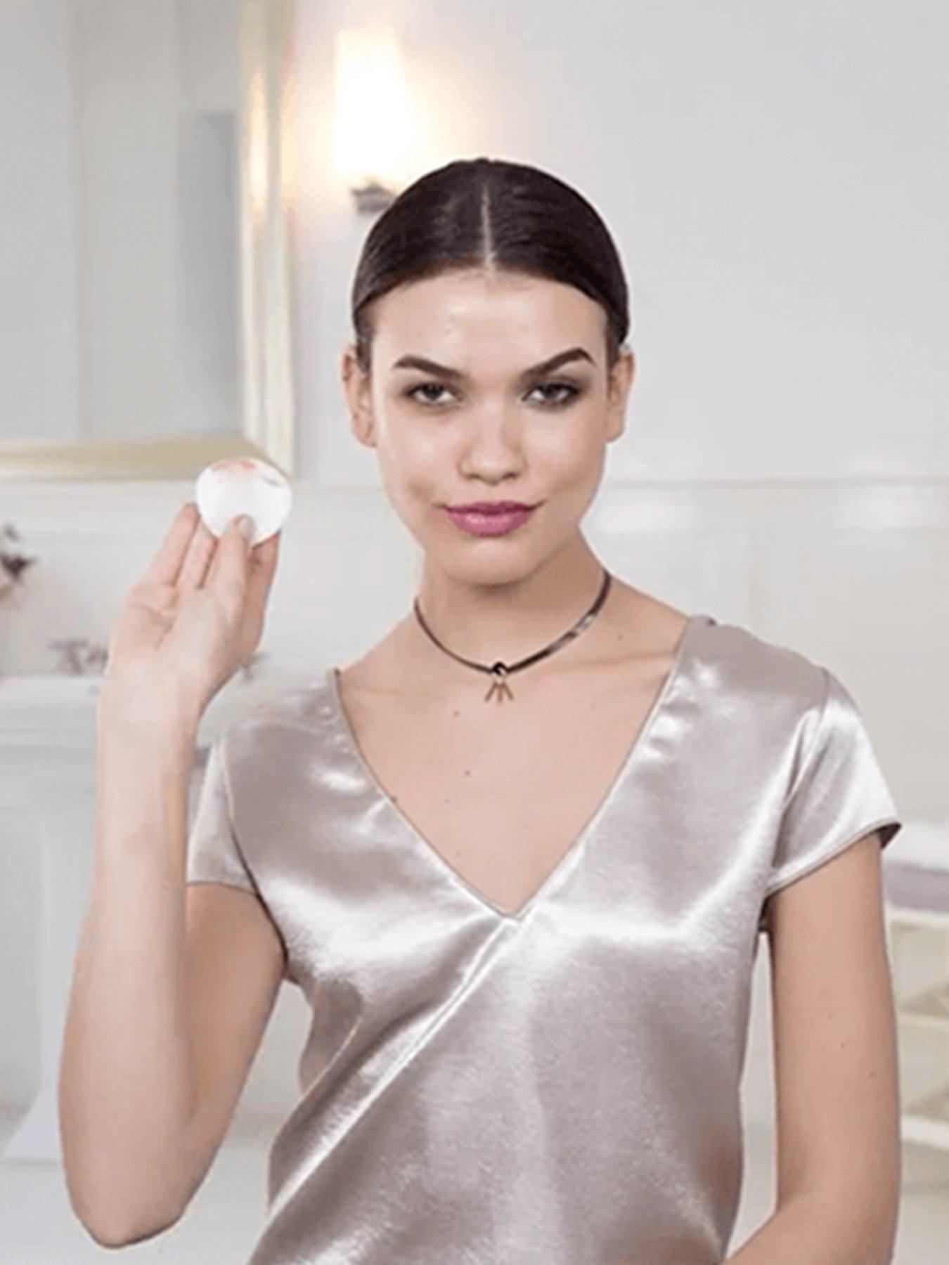 Woman with heavy makeup holds a Micellar Cleansing Water All-in-1 Waterproof pad up, showing the makeup removed from her right eye.